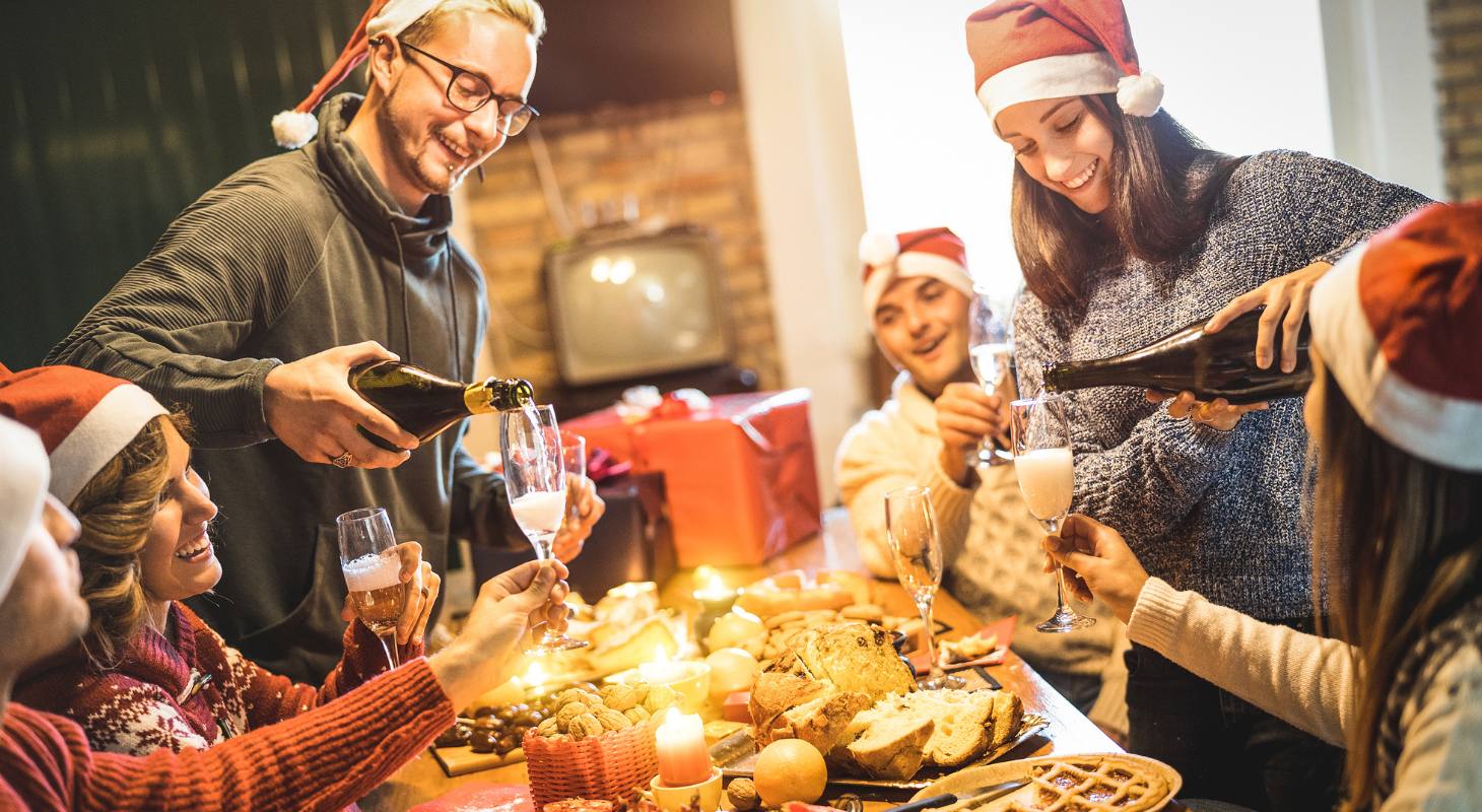 Group of people smiling around a table of food wearing Christmas hats